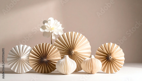 Elegant paper decorations in neutral tones, featuring circular fans and sculptural shapes alongside a delicate flower against a soft background