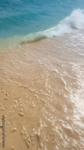 Gentle turquoise ocean wave rolling onto a sandy beach shore creating foamy bubbles in shallow water. Natural idyllic beach scene.