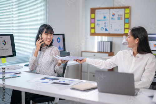 Two women in a cubicle, one of them is talking on the phone
