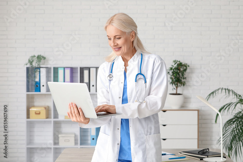Mature female doctor using laptop for telemedicine consultation in modern cli...