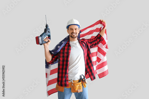 Male worker with USA flag and drill on light background. Labour Day celebration