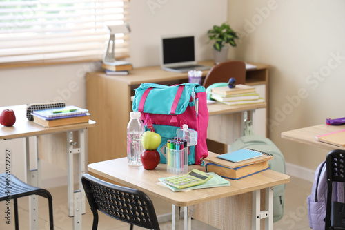 Apples with water bottle and backpack on desk in classroom