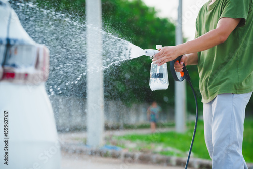 A middle-aged Asian man carefully washes his car using water and foam. Each step from high-pressure rinsing to scrubbing and drying ensures the vehicle is spotless, well-maintained, and presentable