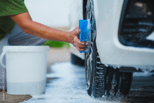 A middle-aged Asian man carefully washes his car using water and foam. Each step from high-pressure rinsing to scrubbing and drying ensures the vehicle is spotless, well-maintained, and presentable
