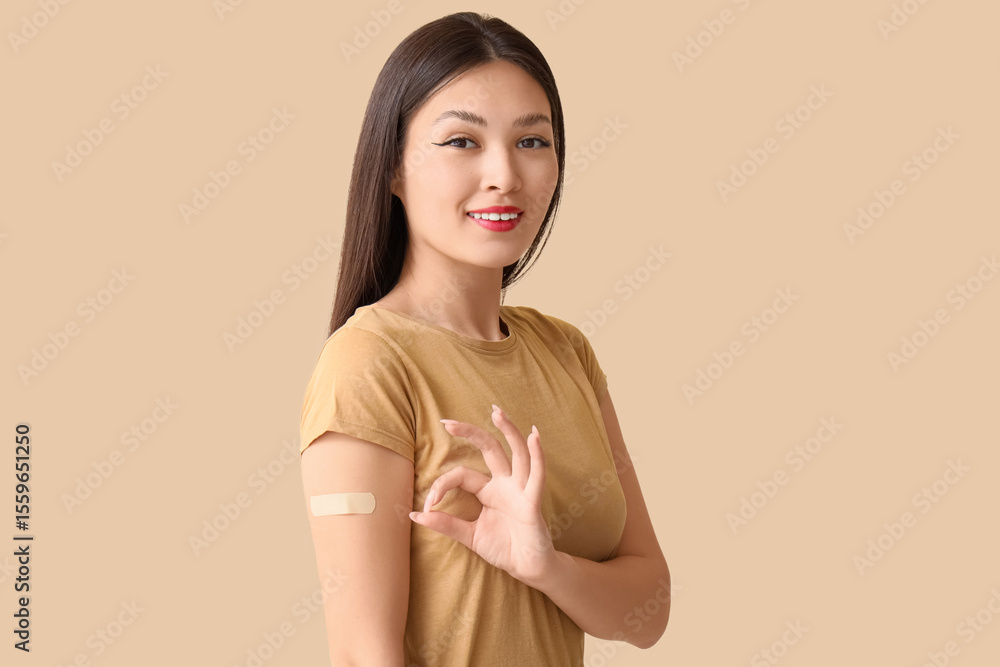 Obraz premium Young Asian woman with applied medical patch showing OK on beige background. Immunization concept
