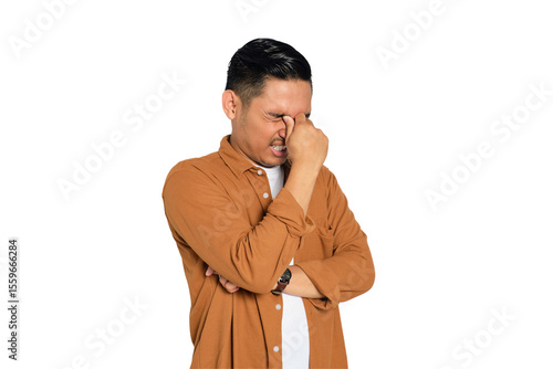 Fotografie Portrait of tired young Asian man in casual shirt rubbing eyes with finger isola