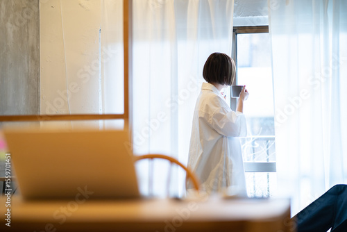 マグカップを持って窓際でリラックスする女性