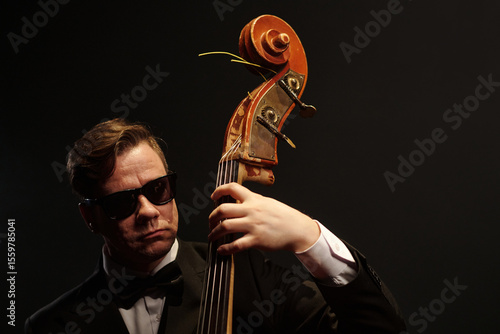 Canvas Print Caucasian middle aged man wearing sunglasses playing double bass on stage, focus
