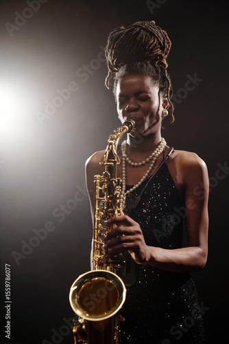 Photography Black young female musician playing saxophone on stage, wearing jewelry and dres