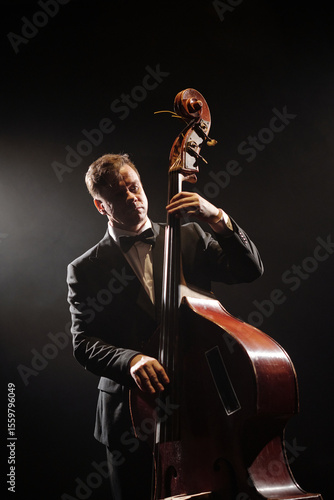 Canvas Print Caucasian middle aged man playing double bass on stage, standing under dramatic