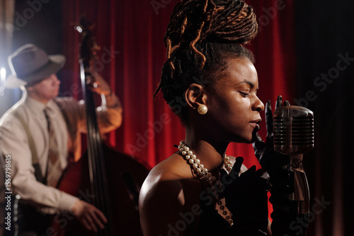 Photography Black young adult woman singing into vintage microphone with eyes closed, wearin