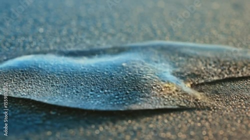A clear liquid being poured onto a dark textured surface creating a small puddle and stream effect