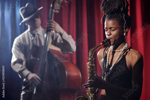 Photography Black young adult woman playing saxophone on stage with eyes closed while Caucas