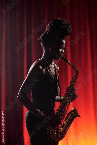 Canvas Print Black woman playing saxophone on stage in front of red curtain, holding instrume