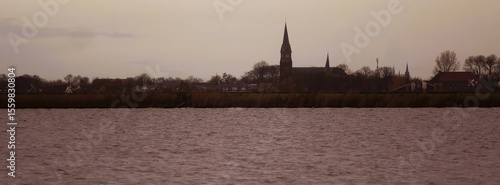 View of the village skyline from Oudega in Frisia Netherlands at dusk with the village church, in the foreground  the lake Aldegeaster Brekken,