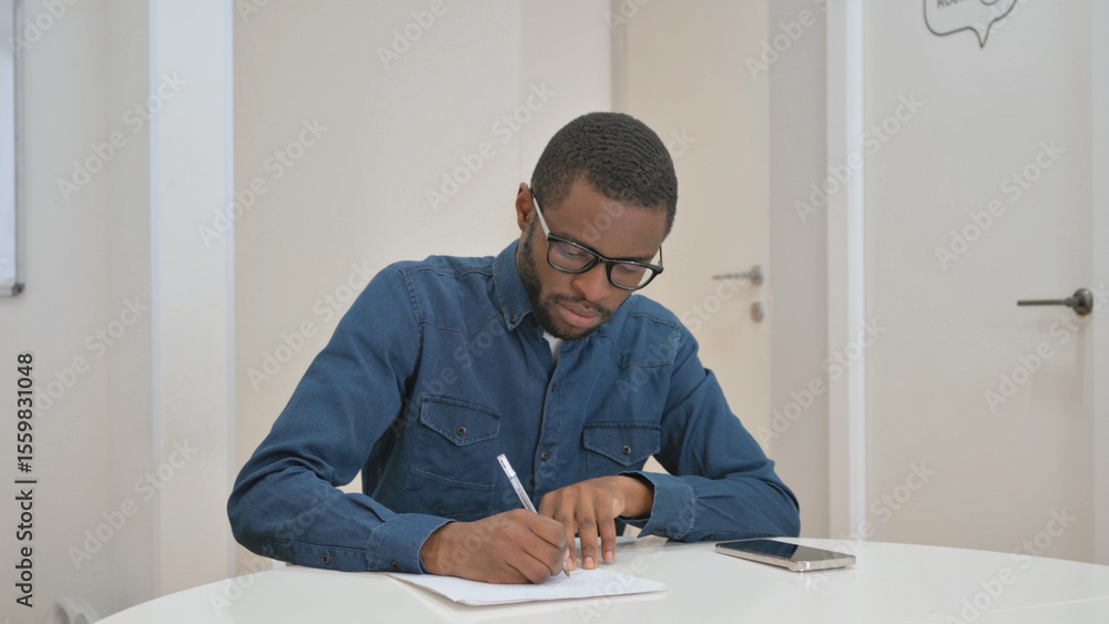 Young African Man Writing while Sitting at Office Young African Man Writing while Sitting at Office