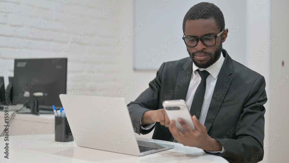 Businessman Using Smartphone While Working on Laptop Businessman Using Smartphone While Working on Laptop