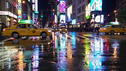 Yellow cabs are driving on a wet times square street at night, reflecting the colorful lights of billboards and advertisements, while pedestrians walk on sidewalks
