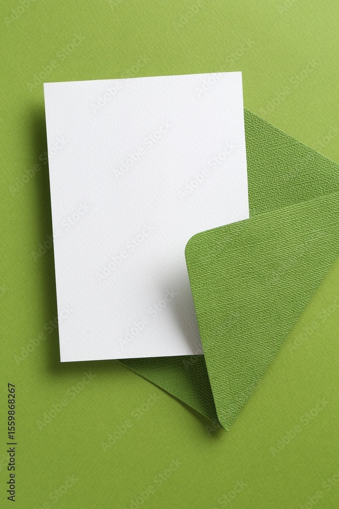 Fototapeta premium Blank invitation card and envelope on green background, top view. Space for design