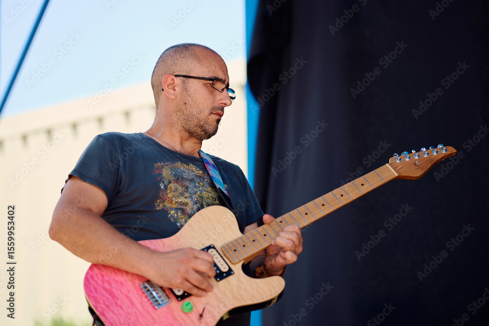 Obraz premium Rock band member performs on stage during outdoor festival in sunny weather