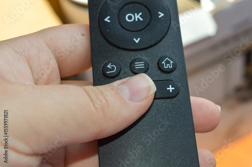 Wallpaper Mural hand holding black remote control with projector box in background — perfect for tech product reviews, user interface, electronics, smart home devices, and remote access control themes Torontodigital.ca