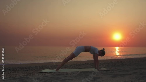 Woman Practicing Downward Facing Dog Yoga Pose at Sunset on Beach