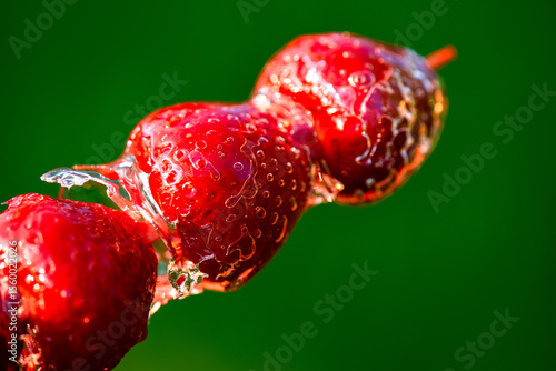 Tanghulu Chinese dessert, stawberry candy on stick coating with sugar caramel glaze on a green, closeup. Strawberries in glass. Popular sweet dish at street food.