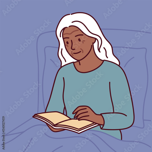 Dark skinned senior woman with white hair reads book peacefully in bed during calm and relaxing evening routine