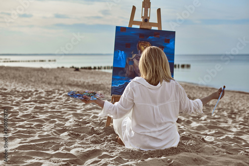 Young woman artist in casual attire sits on sandy beach, painting vibrant seascape on canvas. Serene morning ambiance, with gentle waves and soft light, enhances creativity