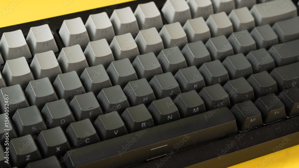Fototapeta premium Minimalist mechanical keyboard with gradient gray keycaps placed on a vibrant yellow background, showcasing a clean, modern, and top-down tech aesthetic
