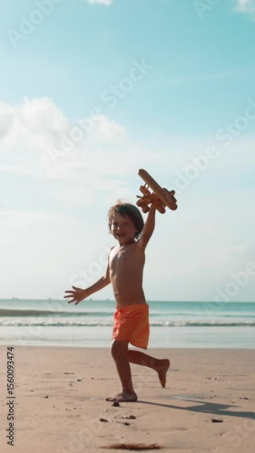 Wallpaper Mural Happy little boy running along seaside with wooden toy airplane in hand, laughing and playing as if plane is flying. Slow motion scene of childhood joy, freedom, imagination and summer adventure on Torontodigital.ca