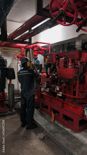 A worker inspects a large red fire pump in a subterranean mechanical room.