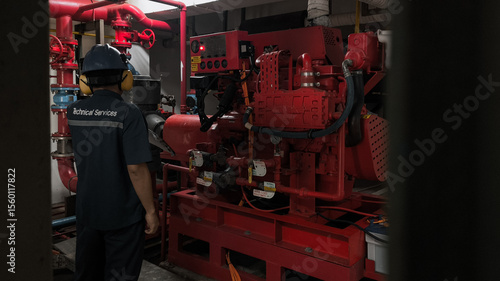 A technician inspects a red fire pump in a confined, dark space.