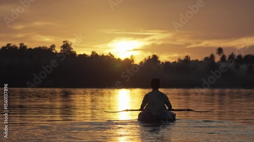 A man paddles a kayak on a tropical island with a sunset in the background. Slow motion video of a man enjoys the sunset while playing kayak