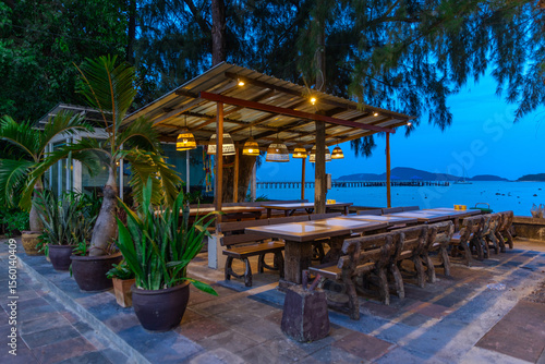 Blue skies at Blue hour Sunset over Rawai Beach in Phuket island Thailand. Restaurants with colourful lanterns lighting up the footpath. Lovely turquoise blue waters, lush green trees 