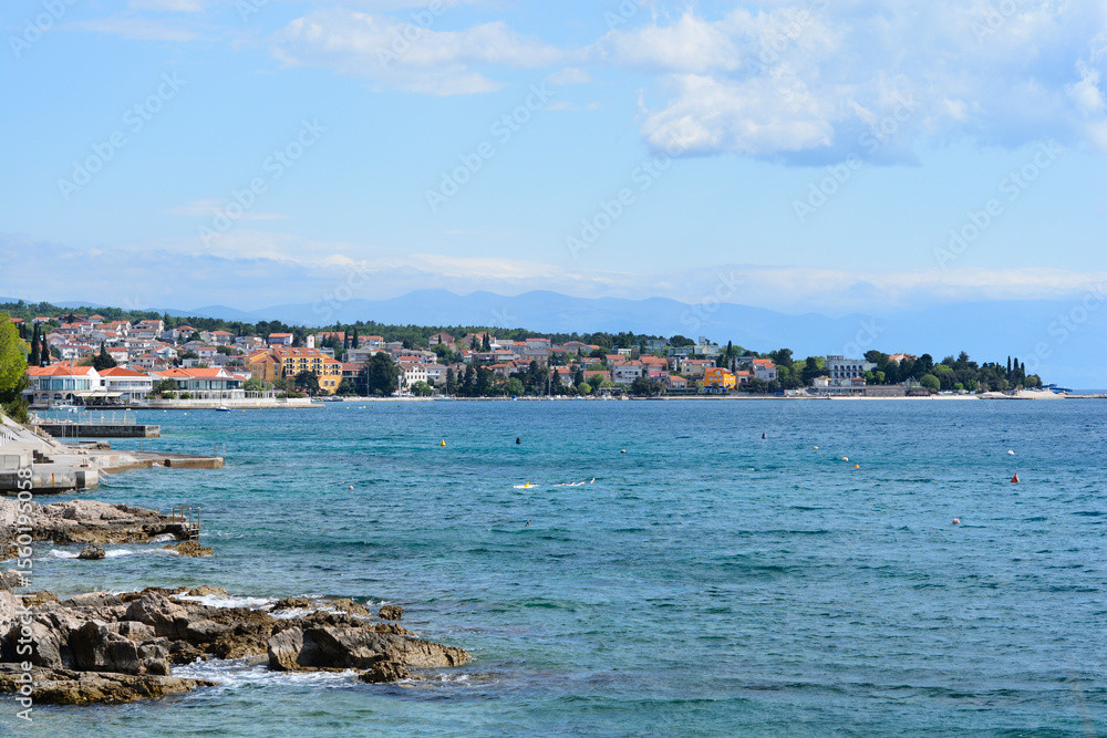 Fototapeta premium A panoramic view of the coastal town of Selce, Croatia, showing its waterfront buildings, the calm blue sea with buoys, and rocky shore