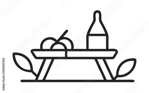 A minimalist picnic setup featuring a fruit bowl and drink on a table surrounded by leaves.