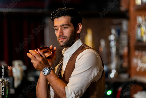 Photography A handsome and focused professional bartender concentrating as he prepares a craft cocktail with a copper shaker in a stylish, dark bar at night