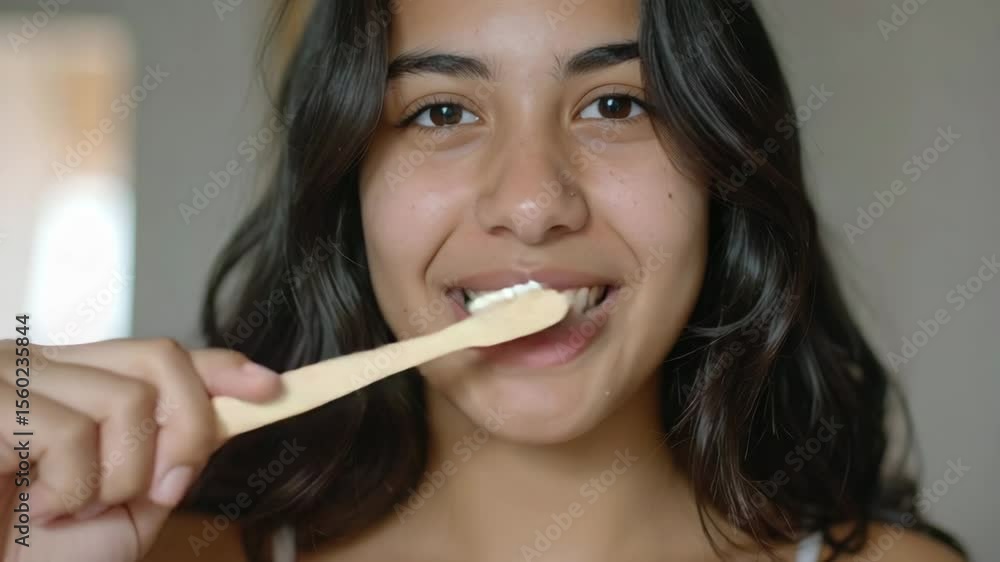 A cheerful young girl with dark hair smiles as she brushes her teeth with an eco-friendly bamboo toothbrush, promoting dental health and wellness. A cheerful young girl with dark hair smiles as she brushes her teeth with an eco-friendly bamboo toothbrush, promoting dental health and wellness.