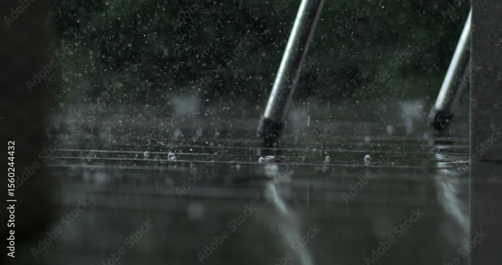 Close up of rain drops bouncing off wet wood near metal chair leg, recorded in super slow motion with high speed camera, garden scene in background