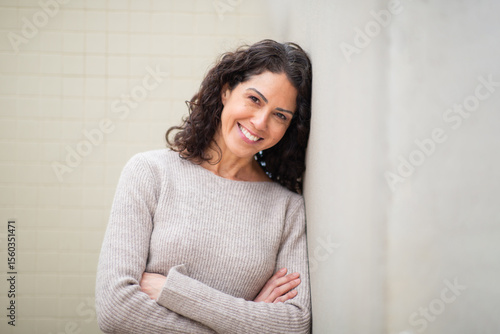 Portrait smiling woman leaning against a wall with arms crossed