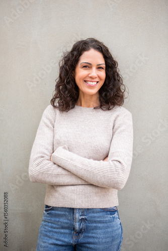 Portrait of a confident woman with curly hair smiling with arms crossed against background