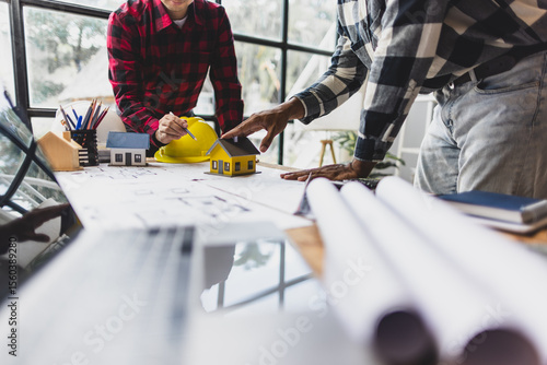 Photography Two architects are discussing a residential housing project, using a model house for reference while reviewing blueprints and taking notes