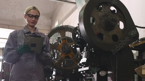 Female lathe operator wearing safety glasses to protect from metal chips while carefully operating metal stamping machine working on thin sheet metal in parts manufacturing plant.