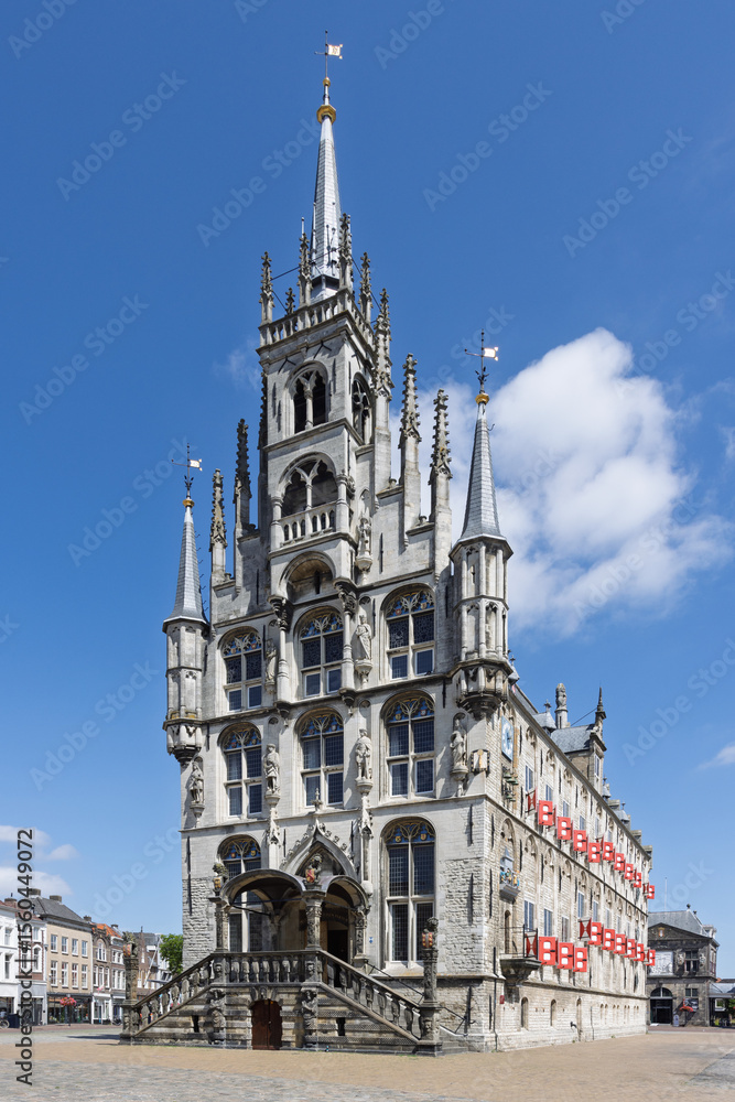Fototapeta premium Stunning Gothic Town Hall of Gouda, Netherlands, adorned with red flags under a clear blue sky, a true architectural masterpiece.