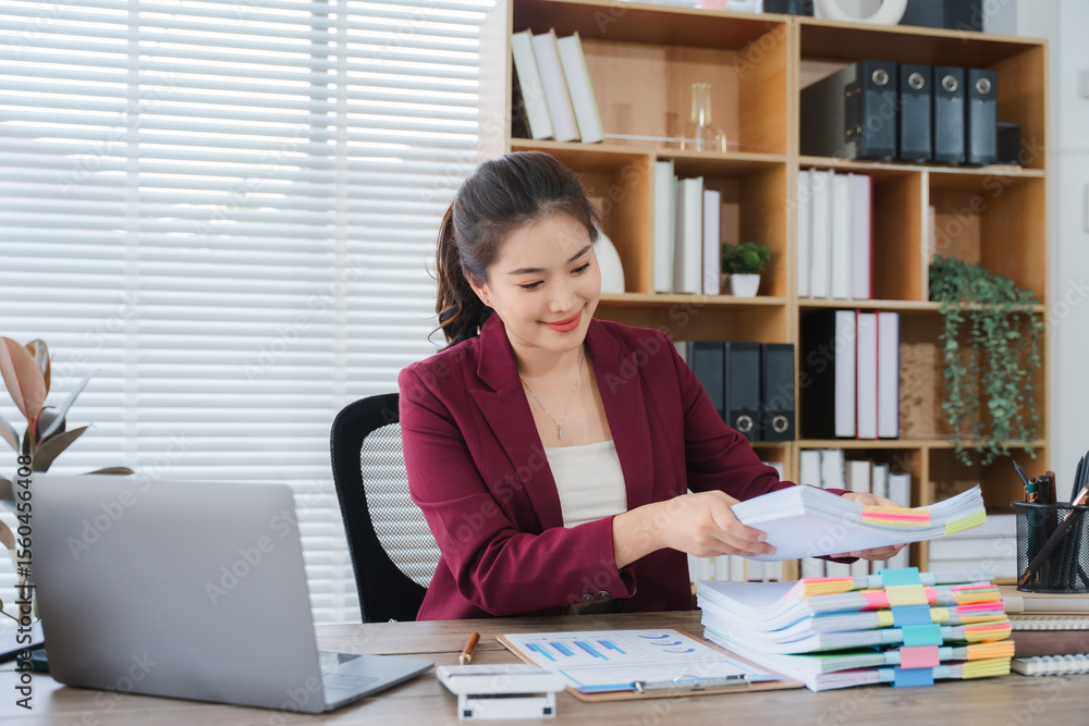 Businesswoman at Work: An elegant businesswoman, immersed in her task, is seen amidst a well-organized office setting with an open laptop, stacks of documents, and a shelf full of reference books. Businesswoman at Work: An elegant businesswoman, immersed in her task, is seen amidst a well-organized office setting with an open laptop, stacks of documents, and a shelf full of reference books.