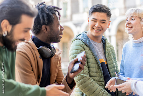 Fotografija Diverse group of young adults socializing with smartphones outdoors in urban set