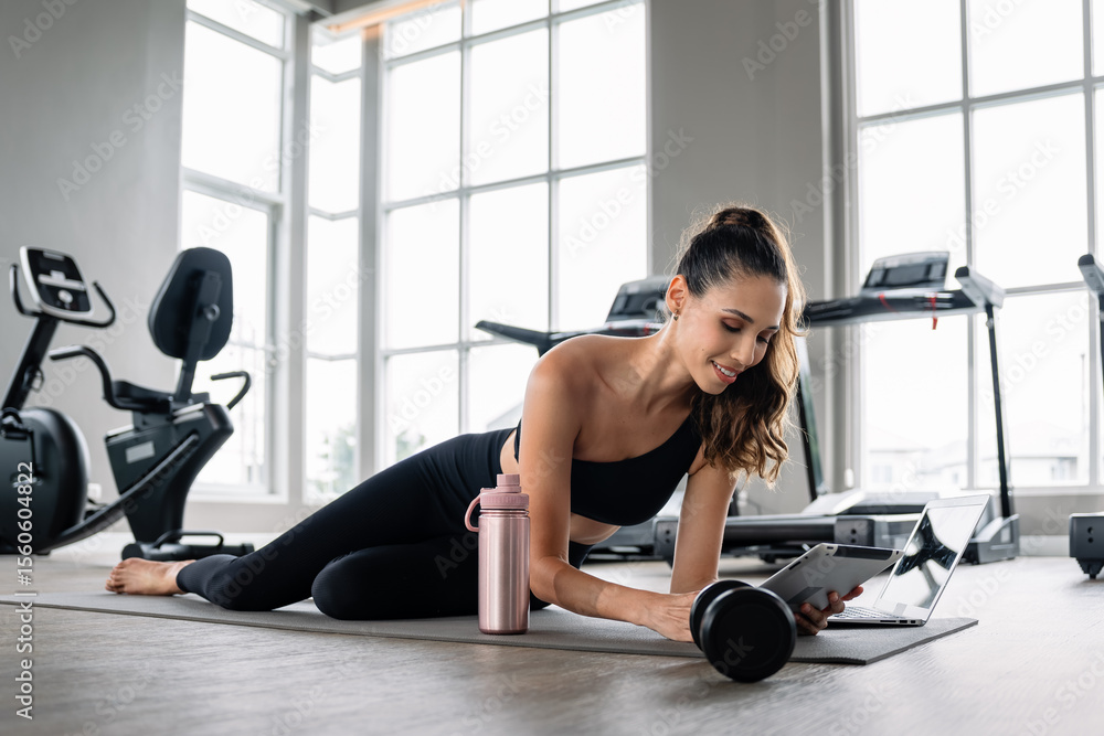 Fototapeta premium A woman is laying on the floor with a laptop and a water bottle. She is smiling. The laptop is open and the water bottle is next to her