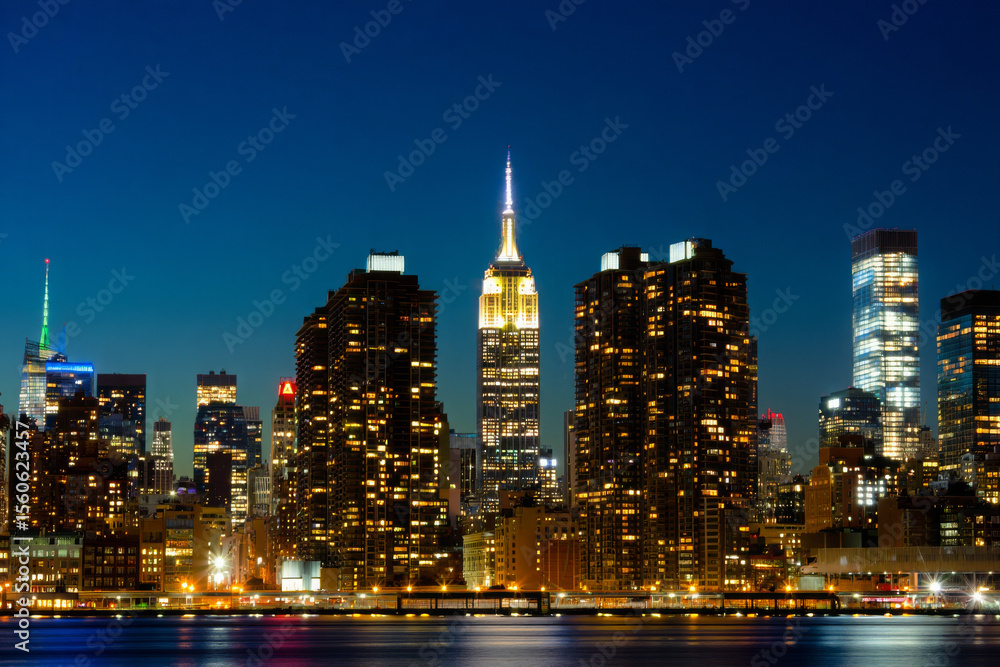 Naklejka premium Vibrant New York City skyline at night with reflections on the water, showcasing urban architecture and towering skyscrapers