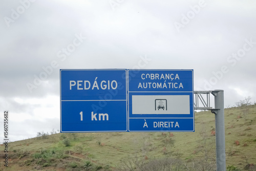 Sinalização rodoviária indicando pedágio a 1 km com opção de cobrança automática à direita. Foto ideal para temas de mobilidade, transporte rodoviário e infraestrutura no Brasil.